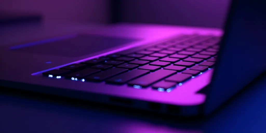 a close up of a laptop keyboard with a logo on it's side and a purple light shining on the keyboard,