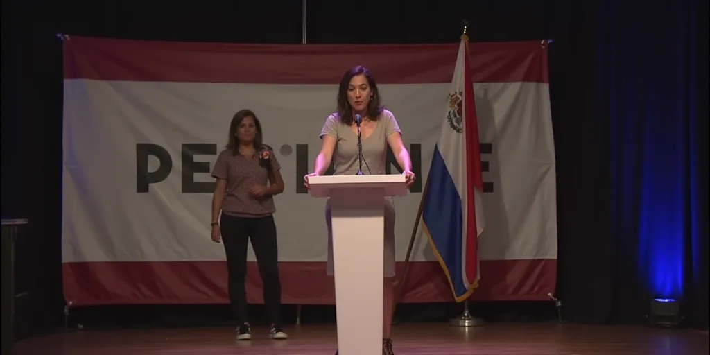 a woman standing at a podium in front of a banner and a flag on a stage with a woman standing at a p