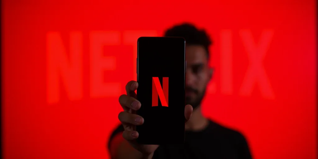 a person holding a cell phone with a netflix logo on it in front of a red background with a netflix