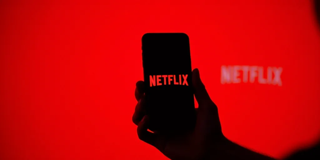 a person holding a cell phone with a netflix logo on it in front of a red background with a netflix