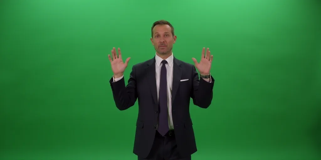 a man in a suit and tie making a gesture with his hands while standing in front of a green wall, Art
